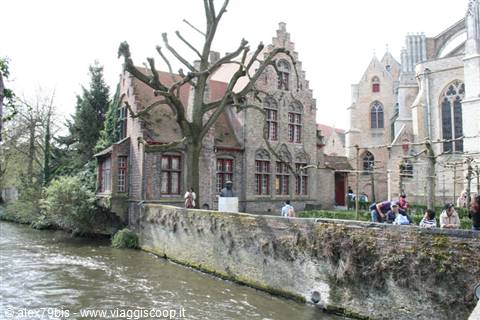 Stepped brick houses along a canal, people sitting on the wall, Bruges