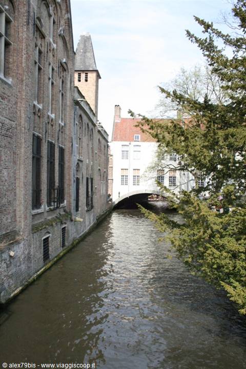 Bruges canal between brick houses, stone bridge and bell tower in daylight