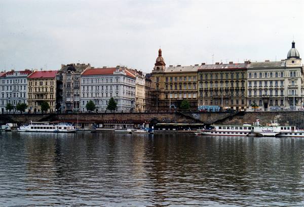 Historic buildings along the Vltava riverbank in Prague, boats moored at the quay