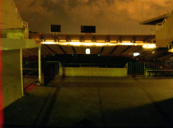 Stadium at night, stands lit by yellow lights, dark pitch