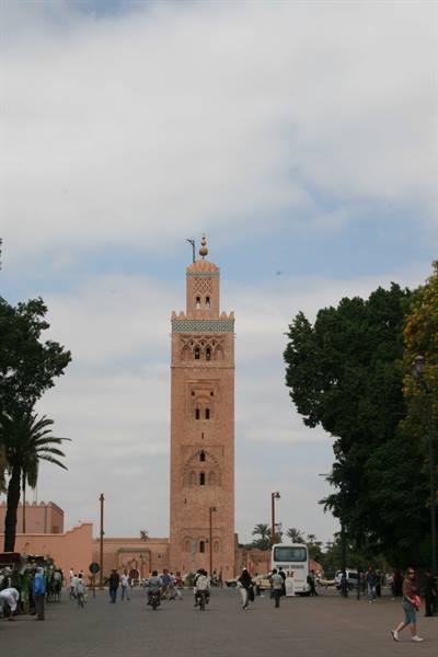 The Koutoubia minaret in Marrakech among trees and traffic under clouds