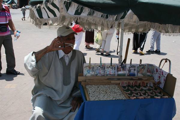 Man in cap drinking from small glass beside stall of trinkets