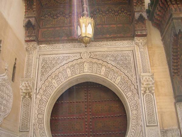 Carved stucco horseshoe-arch doorway with brass lantern in Fez medina