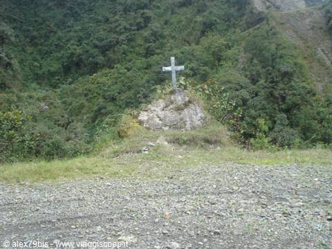 White concrete cross on grassy ledge, forested hills behind