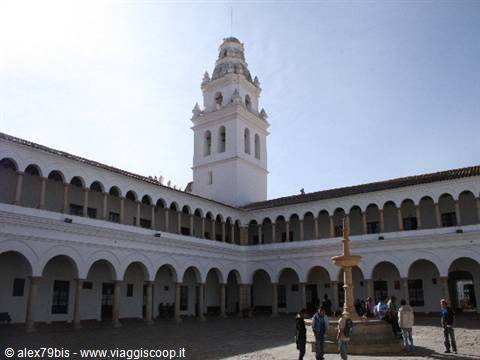 White arched cloister with bell tower and central fountain, tourists below
