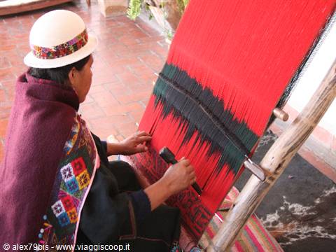 Andean weaver in white hat weaving red threads on a wooden loom