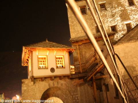Stone tower with lit windows beside an old bridge at night