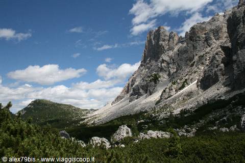 Dolomite rock wall towers over green shrubs under blue cloudy sky