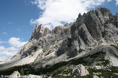 Jagged dolomite peaks above pine trees and scree, white clouds