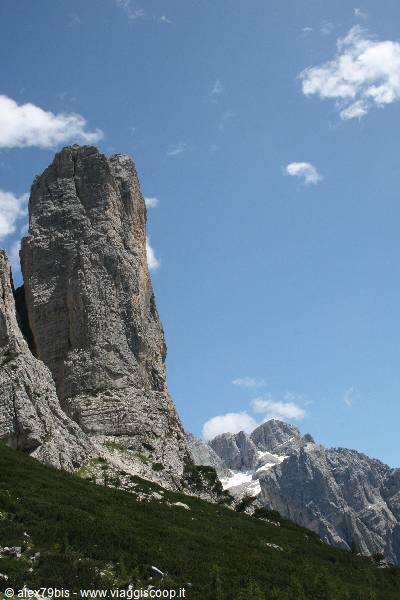 Dolomite rock tower rising above green slopes, blue sky with clouds