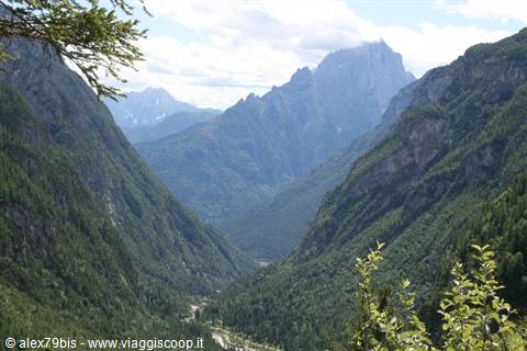 Forested valley with winding roads below, jagged rocky peaks in clouds, Dolomites
