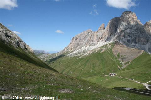 Dolomite peaks above green meadows, a hut and road in the sunny valley