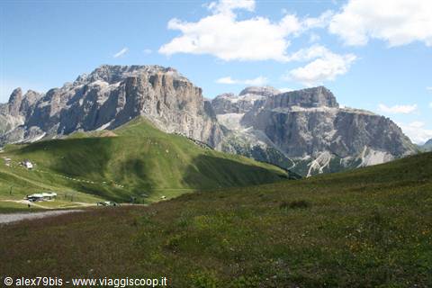 Green meadows beneath the rugged Sella Dolomite peaks, blue sky with clouds