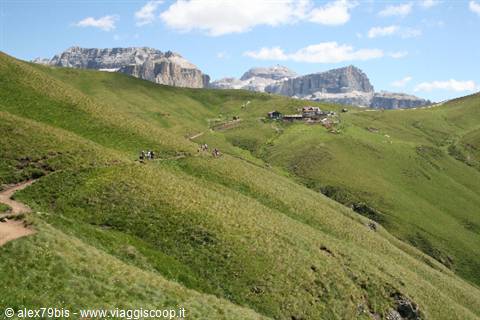 Hikers on grassy trail toward mountain hut, Dolomites peaks in background