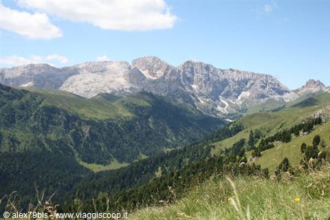 Dolomite peaks above green pastures and forests, white clouds