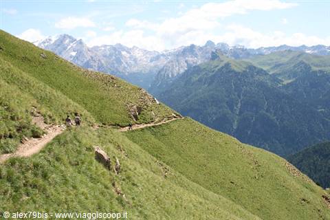 hikers on grassy mountain trail with green slopes and rocky peaks