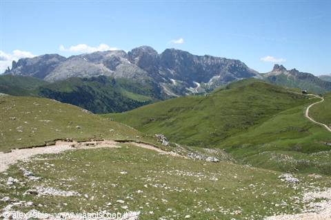 Green meadows and trail beneath the rocky Sella Dolomites, blue sky