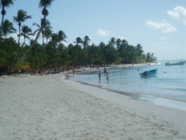 White sand beach with palm trees, swimmers and a blue boat in turquoise water