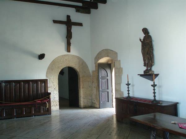 Wooden crucifix and statue on white walls, stone arches and antique furniture