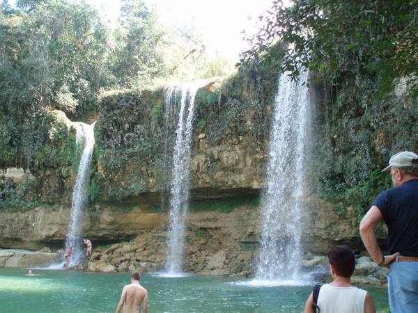 Tourists watch Salto de Eyipantla waterfalls among greenery, some swimming in the pool below