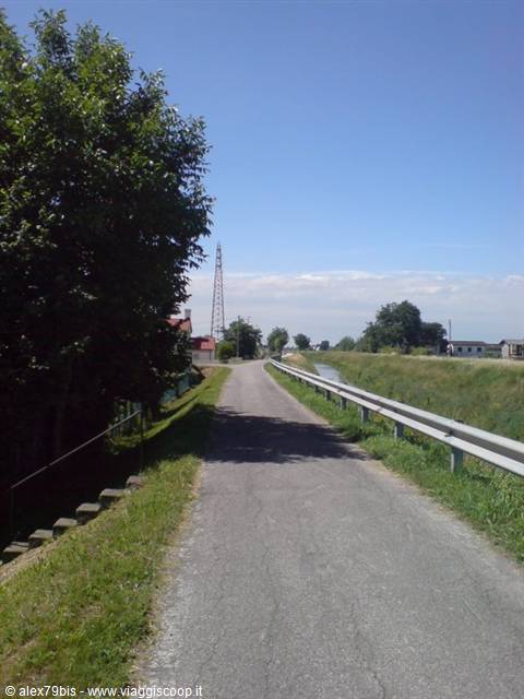 Paved road along a canal, metal guardrail and trees under blue sky