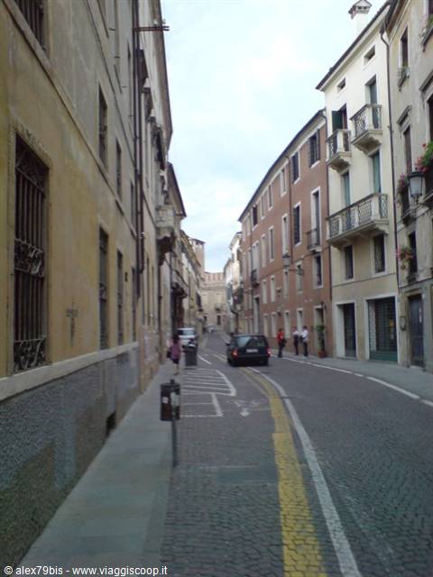 Cobbled street lined with old buildings, people walking past parked cars