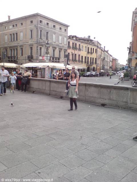 Woman poses on stone pavement in front of colorful buildings and market stalls