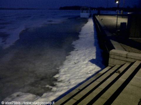 Stone pier with steps, snow and ice on the water, moored boat at night