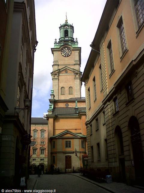 The green bell tower of Storkyrkan cathedral between yellow buildings in Stockholm