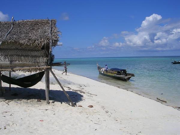 Wooden boat at the shore, thatched hut and hammock on white sand