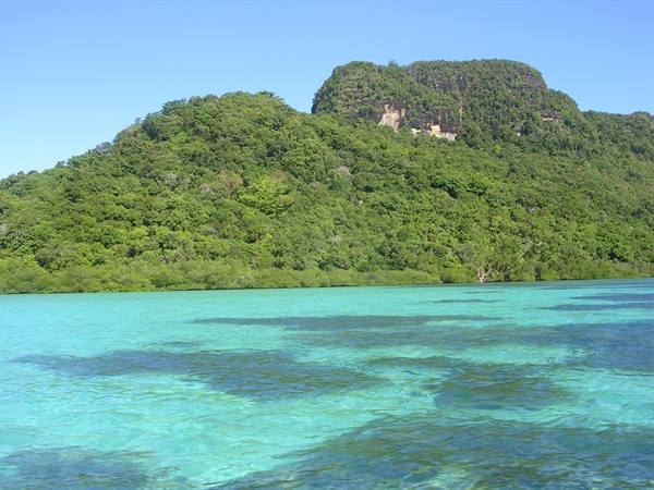 Clear turquoise water in front of green tropical hills covered in jungle