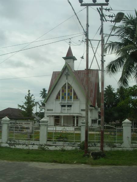 White church with red roof and stained glass, fence and power poles, cloudy sky