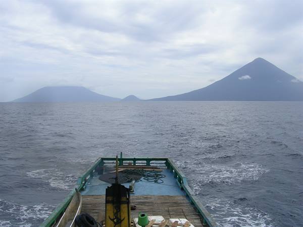 Green wooden boat bow crossing the ocean toward misty volcanic islands