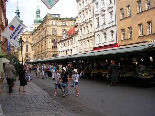 Tourists stroll past open-air market stalls on Havelská street, Prague
