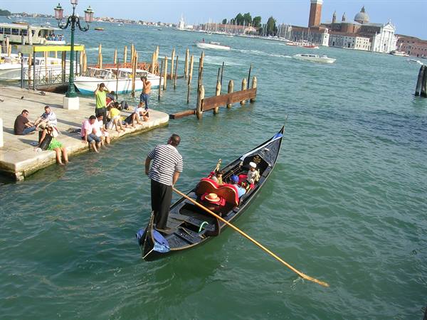 Gondolier rows tourists past wooden mooring poles, Venice