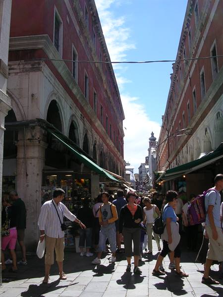 Crowd of tourists walking under red Rialto market arcades in Venice