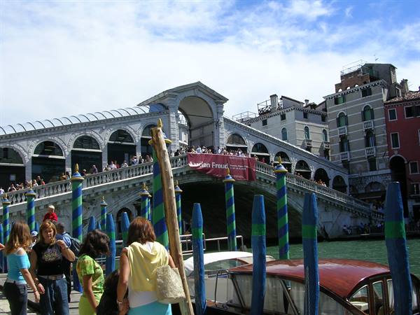 Tourists on Rialto Bridge in Venice among striped poles and canal