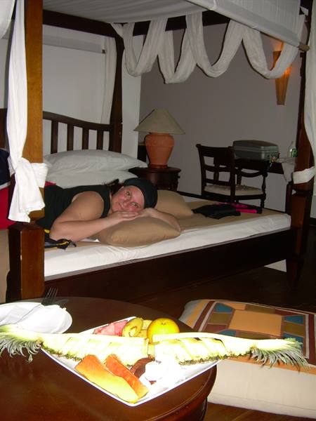 Woman lying on wooden canopy bed, fresh cut fruit on the table