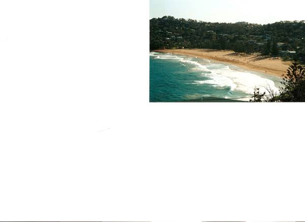 White waves breaking on a sandy beach, houses among green forested hills