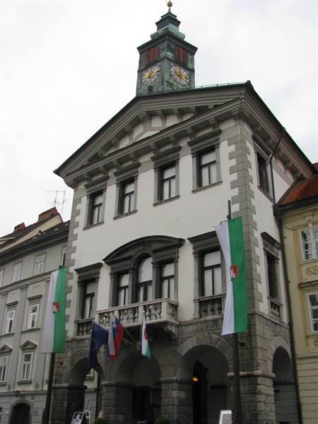 Ljubljana Town Hall with green clock tower and flags beneath a grey sky