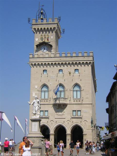 Tourists walk in front of the Public Palace of San Marino under blue sky