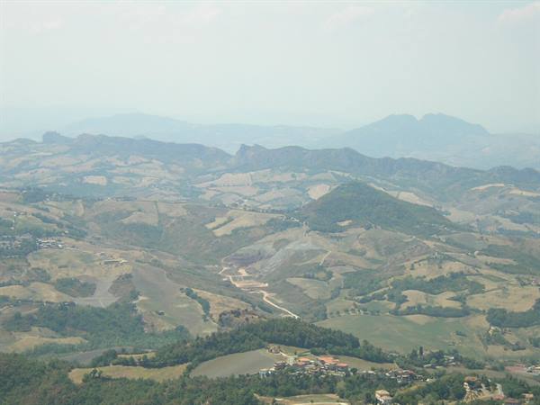 Cultivated hills and woods under haze, with a small village below