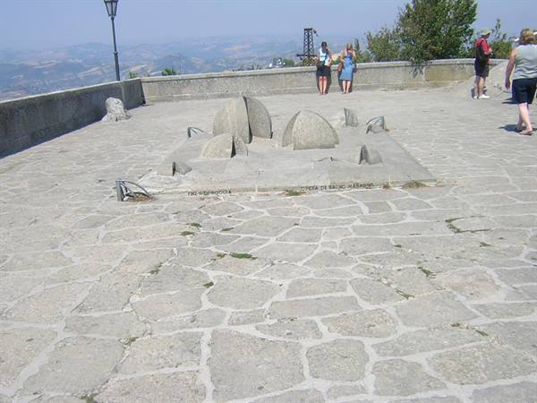 Tourists on paved terrace with a stone sundial, hills in background