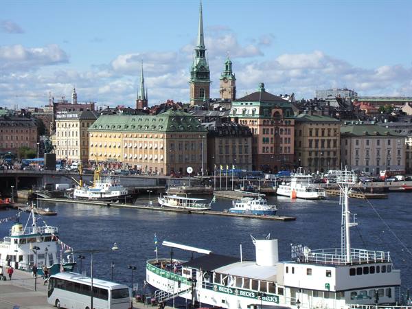 Ferries moored in Stockholm harbor among old buildings and spires under summer sun