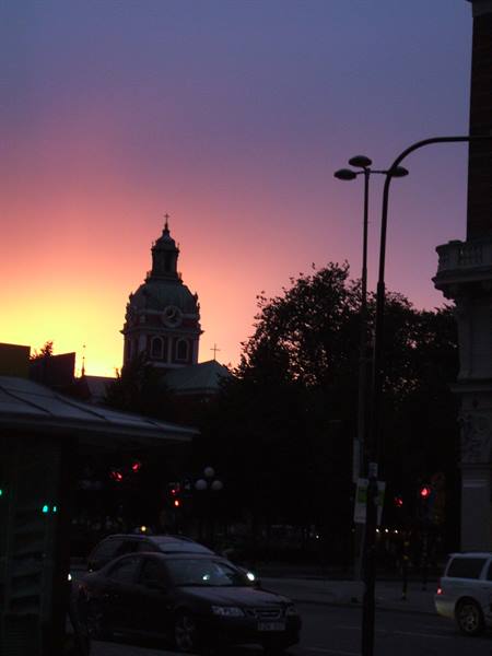 Baroque tower silhouetted at dusk, cars and traffic lights in the foreground