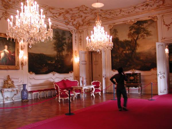 Visitor in a baroque hall with crystal chandeliers, painted wall panels and red sofas