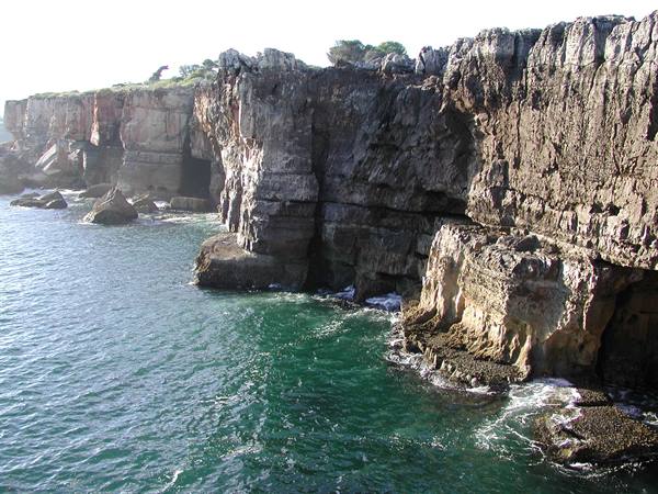Limestone cliffs plunging into emerald sea, wave-carved caves at Boca do Inferno