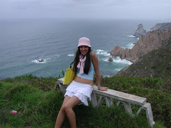 Girl sitting on a stone bench at Cabo da Roca, Atlantic cliffs below