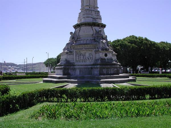 Carved stone base of a marble monument among green hedges in Lisbon