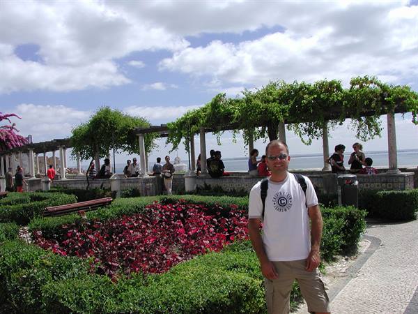 Tourist at Santa Luzia viewpoint in Lisbon, among pergola and red flowerbeds